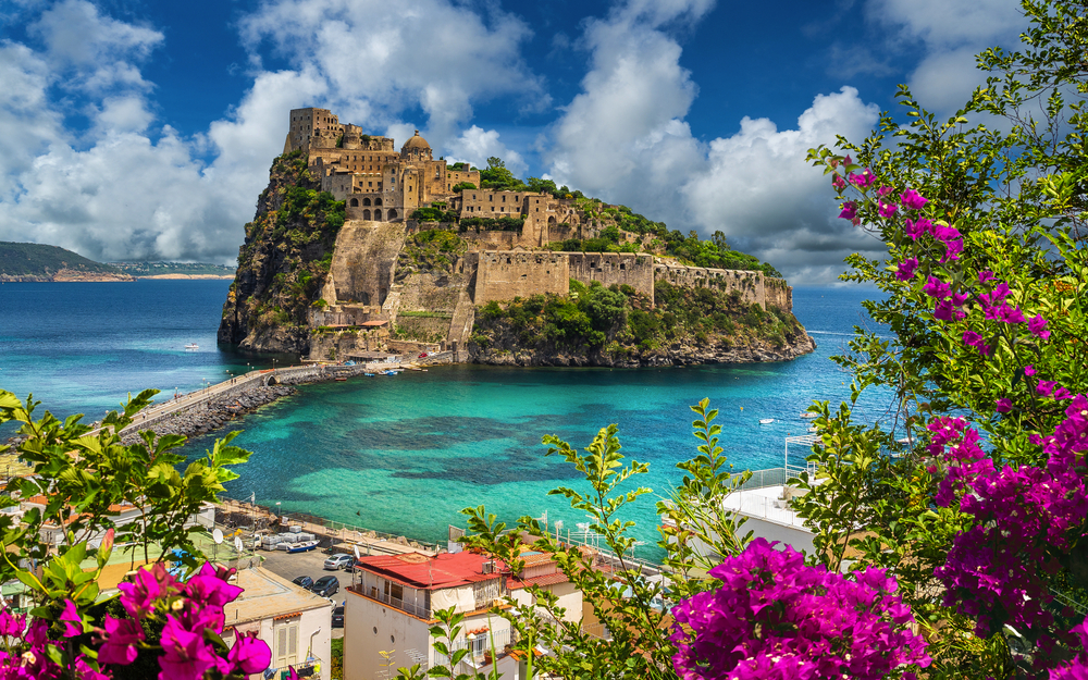 Mittelalterliche Festung auf einer Insel im türkisfarbenen Meer, umgeben von Blumen.