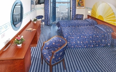 Hotelzimmer mit blauen Betten, Balkon mit Meerblick, Holzschreibtisch, runder Spiegel.