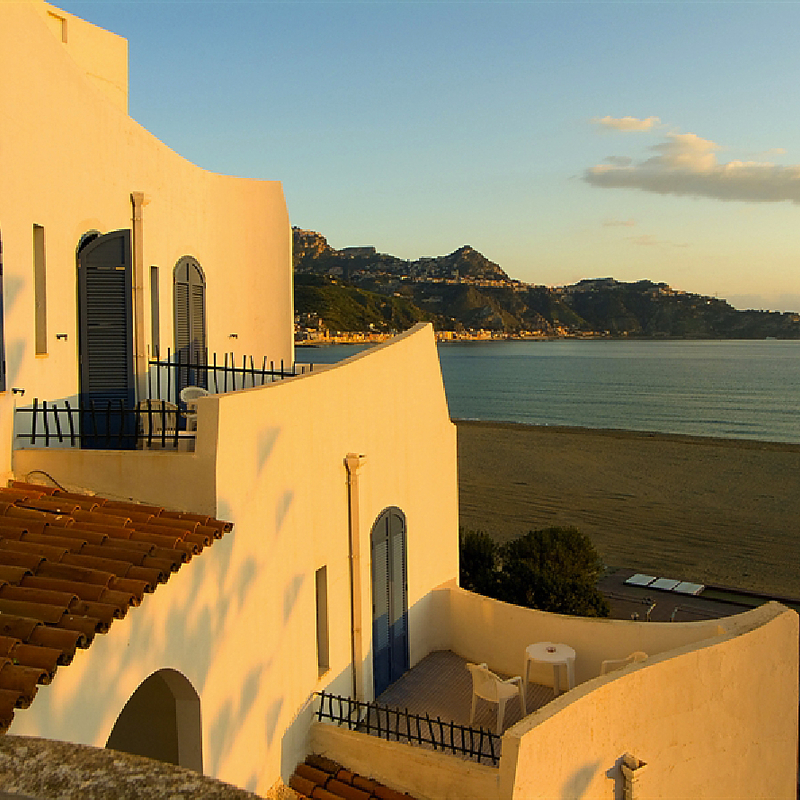 Hotel im mediterranen Stil mit Blick auf das Meer bei Sonnenuntergang.