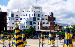 Hotel am Strand mit gestreiften Sonnenschirmen, dahinter Gebäude und Bäume.