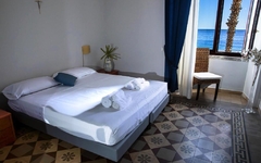 Hotelzimmer mit Doppelbett, Meerblick, Balkon und gefliesten Boden in Sizilien.