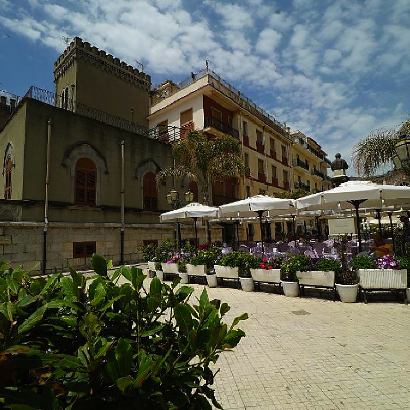 Historisches Gebäude mit Terrasse und Sonnenschirmen in Letojanni, Sizilien.