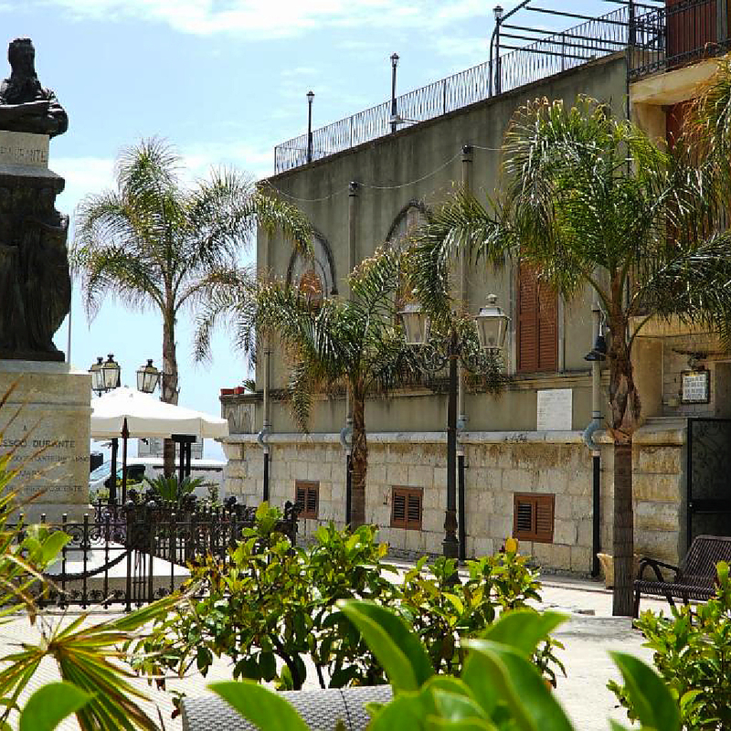 Hoteleingang mit Palmen und Statue in Letojanni, Sizilien.