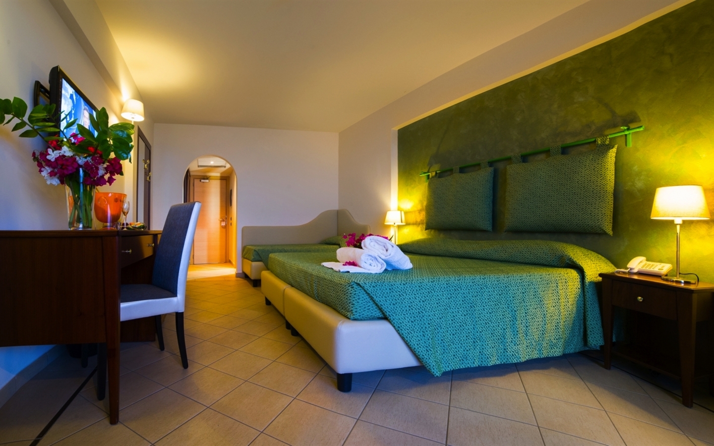 Blick in ein modernes Hotelzimmer mit grünem Doppelbett und Schreibtisch.