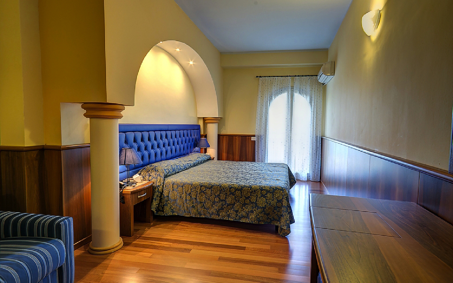 Hotelzimmer in Sizilien mit Doppelbett und Balkon, warmes Licht und Holzboden.