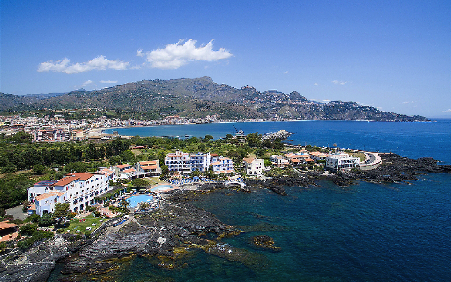 Küstenblick auf Hotel und Meer in Giardini Naxos, Sizilien, umgeben von Bergen.