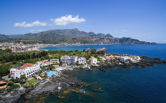 Küstenblick auf Hotel und Meer in Giardini Naxos, Sizilien, umgeben von Bergen.