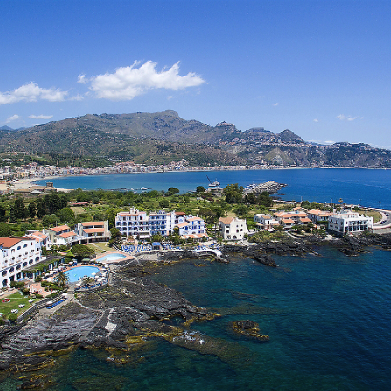 Küstenblick auf Hotel und Meer in Giardini Naxos, Sizilien, umgeben von Bergen.