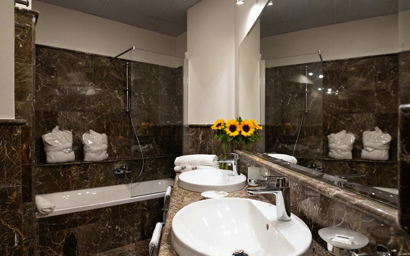 Badezimmer mit Waschbecken, Spiegel, Badewanne und Blumenvasen.