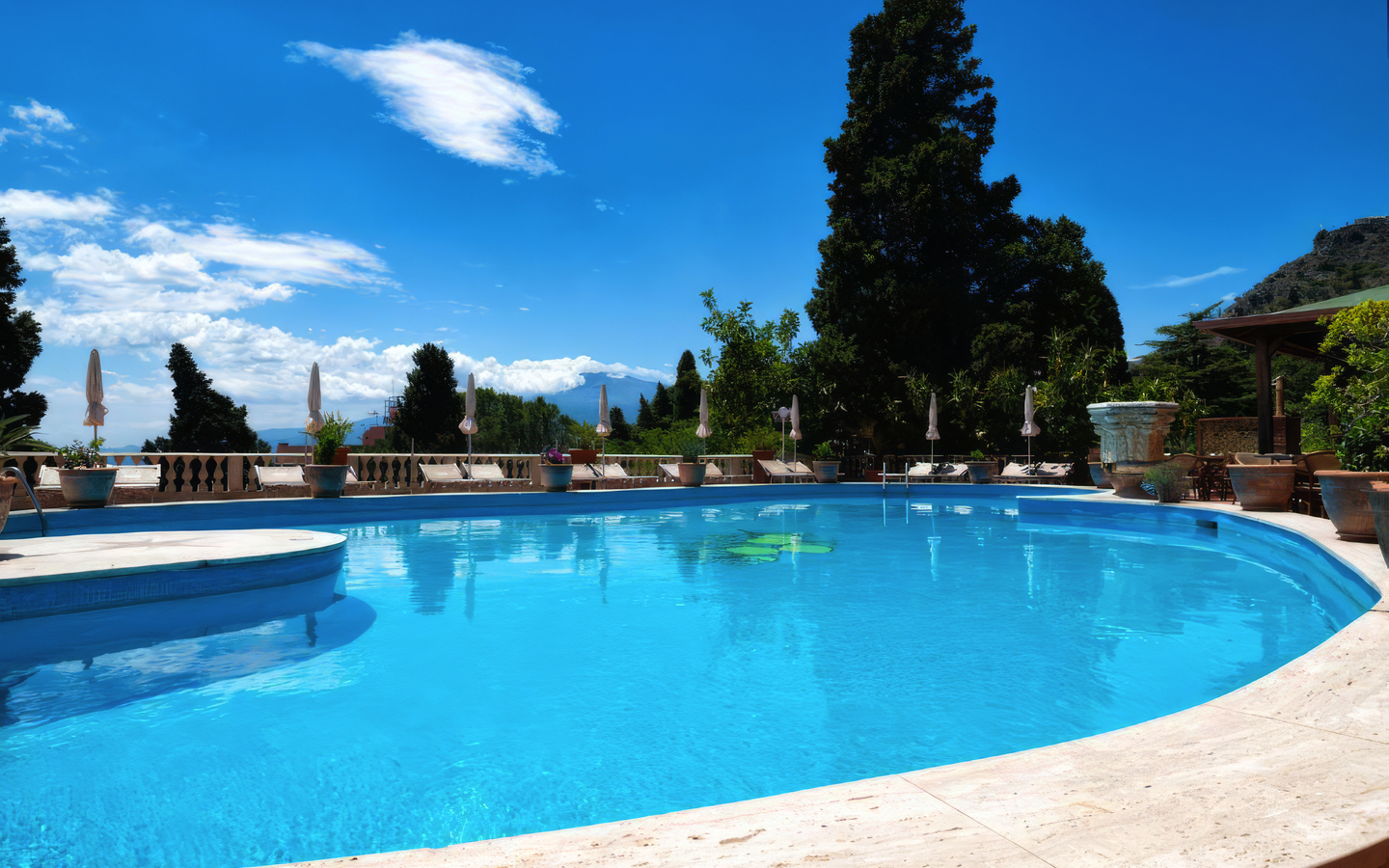 Pool mit Liegestühlen und Bäumen im Hotel Taormina Park, Sizilien.