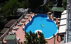 Poolbereich des Hotels Taormina Park auf Sizilien, umgeben von Liegestühlen und grüner Umgebung.