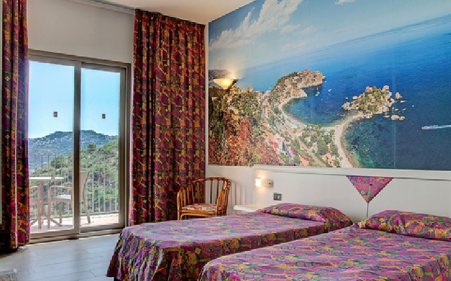 Hotelzimmer mit zwei Betten, bunten Vorhängen und Wandbild von einer Küstenlandschaft