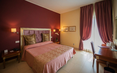 Doppelzimmer mit rosa Wänden und beigefarbenem Bett im Hotel auf Sizilien.