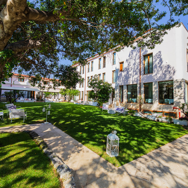 Außenansicht eines Hotels mit Garten und Bäumen im Sonnenschein.