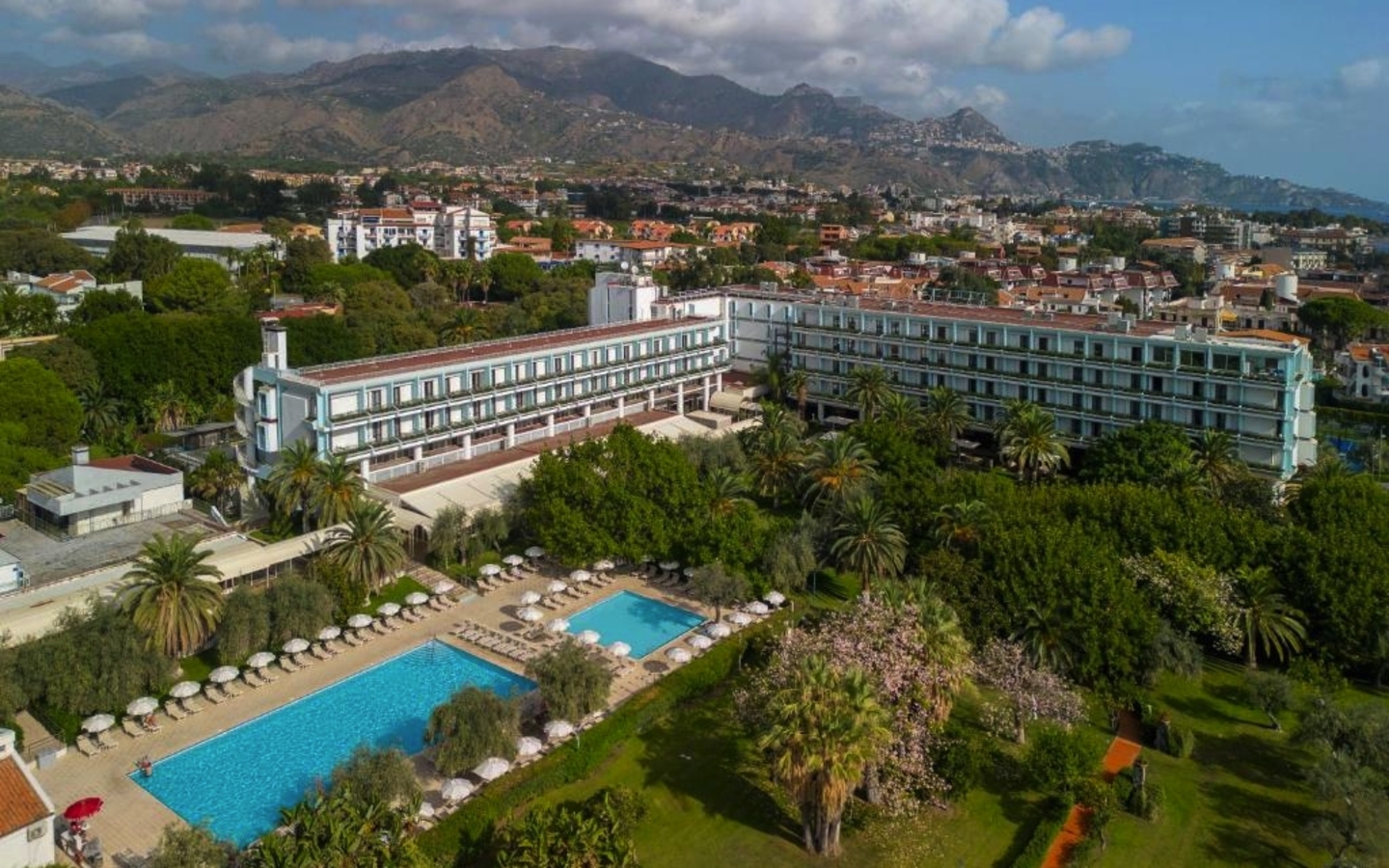 Hotel mit Pool und Garten aus der Luft, Berge im Hintergrund.