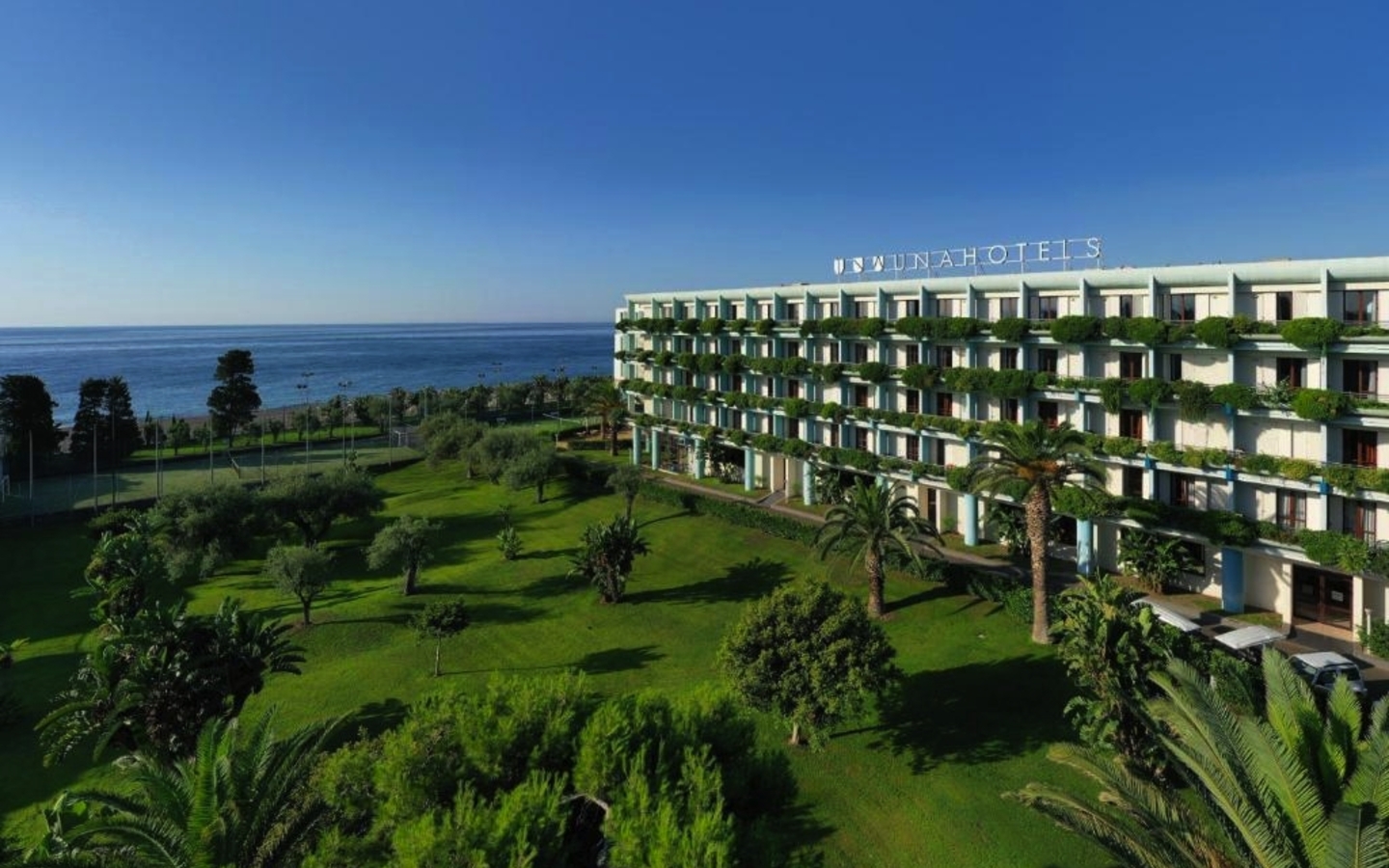 Hotelgebäude am Meer mit großer Gartenanlage und Palmen, Sizilien.