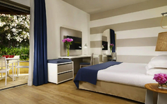 Modernes Hotelzimmer mit Doppelbett, Schreibtisch und Zugang zu einer Terrasse mit Gartenmöbeln.