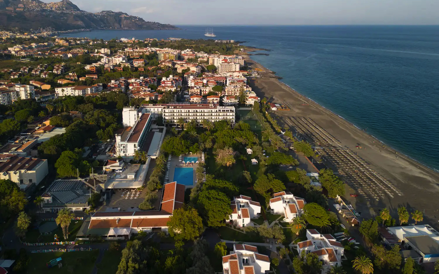 Luftaufnahme eines Küstenhotels mit Strand und umliegender Stadt in Sizilien.