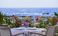 Tisch mit Meerblick, umgeben von Blumen, mit Boot im Hintergrund an einem sonnigen Tag