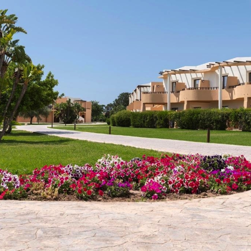 Gartenanlage mit blühenden Blumen vor einem Resort-Gebäude.