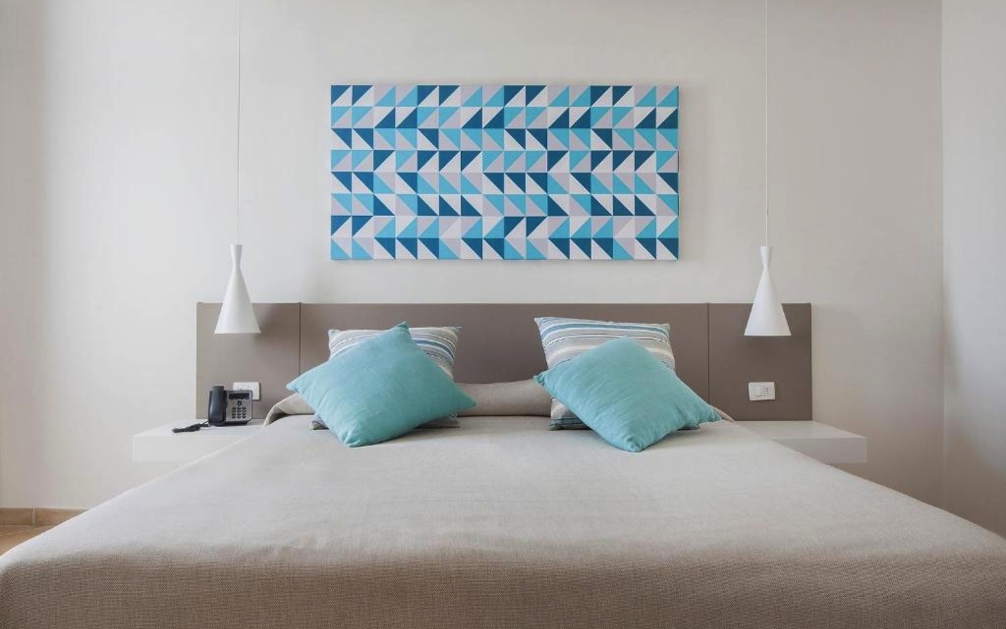 Doppelzimmer mit weißem Bett, blauen Kissen und modernem Kunstwerk an der Wand.