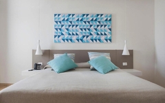 Doppelzimmer mit weißem Bett, blauen Kissen und modernem Kunstwerk an der Wand.