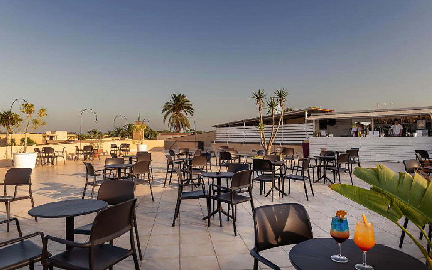 Offene Terrasse mit mehreren Tischen und Stühlen, dahinter eine Bar.