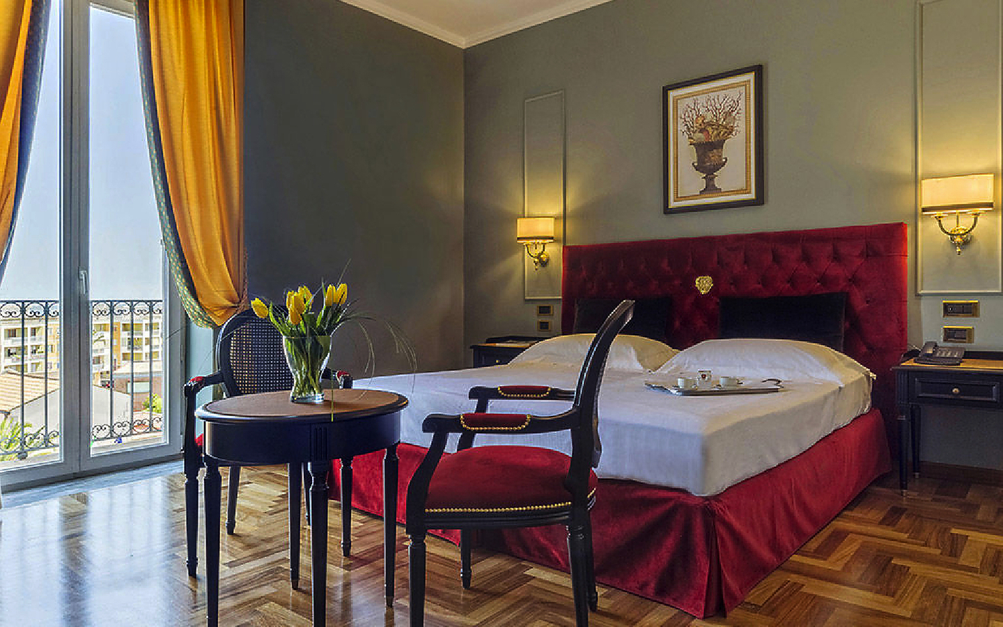 Elegantes Hotelzimmer mit Doppelbett, rotem Kopfteil und Tisch mit Stühlen.