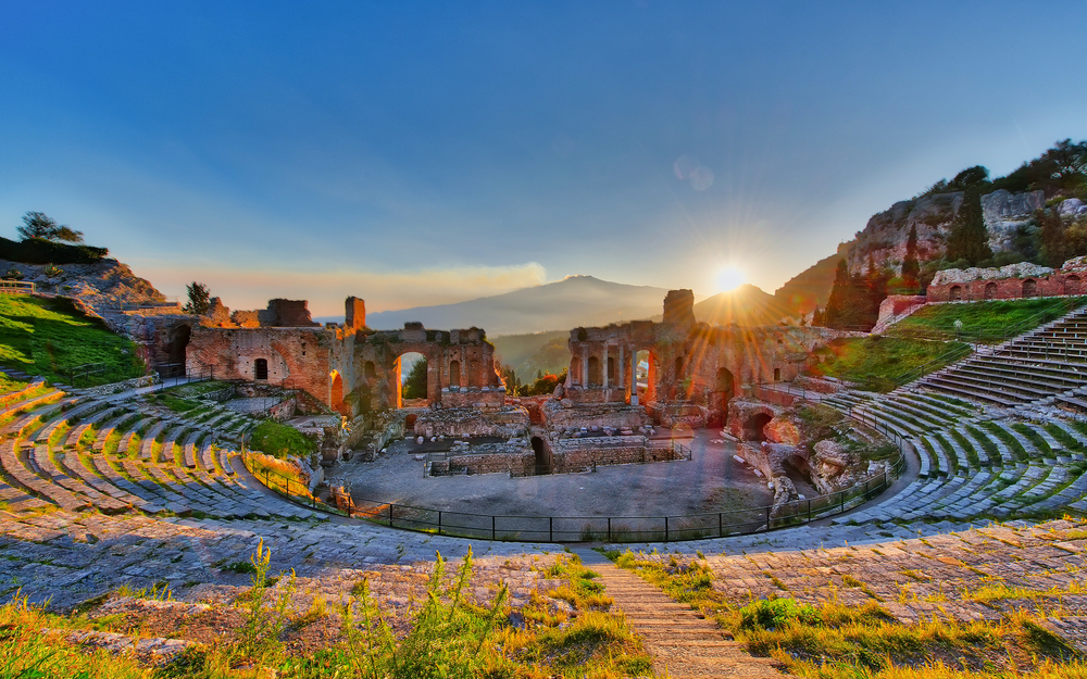 Antikes Amphitheater bei Sonnenuntergang mit Berg im Hintergrund.