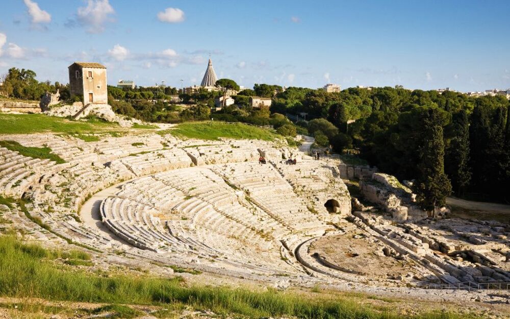 Altes römisches Amphitheater mit Bäumen im Hintergrund unter blauem Himmel.