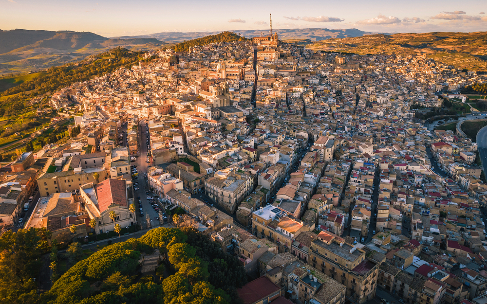 Luftaufnahme einer historischen Stadt mit dicht bebauten Häusern und hügeliger Landschaft.