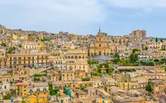 Panorama von Modica, Sizilien mit historischen Gebäuden und hügeliger Landschaft.