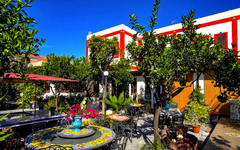 Garten eines Hotels mit bunten Tischen und üppiger Vegetation bei sonnigem Wetter
