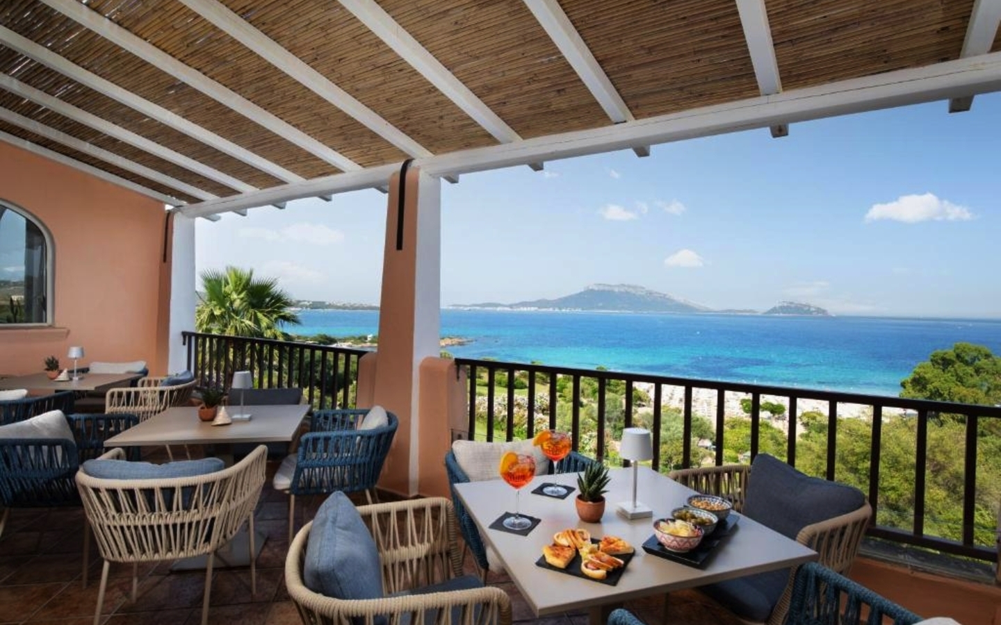 Hotelterrasse mit Tischen und Stühlen, Meerblick im Hintergrund.
