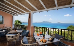 Hotelterrasse mit Tischen und Stühlen, Meerblick im Hintergrund.