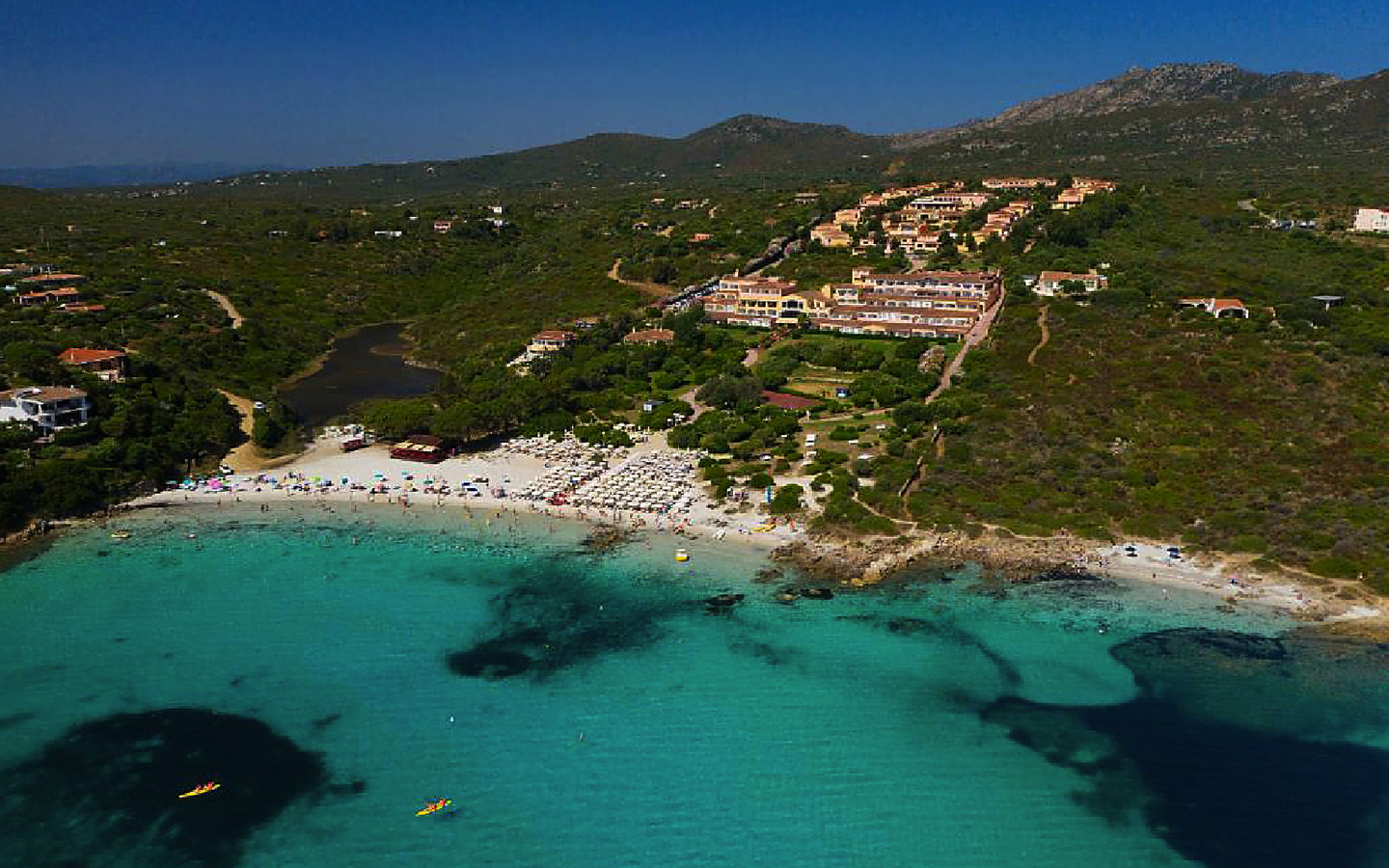 Luftaufnahme einer Hotelanlage in Sardinien, umgeben von grüner Landschaft und Küste.