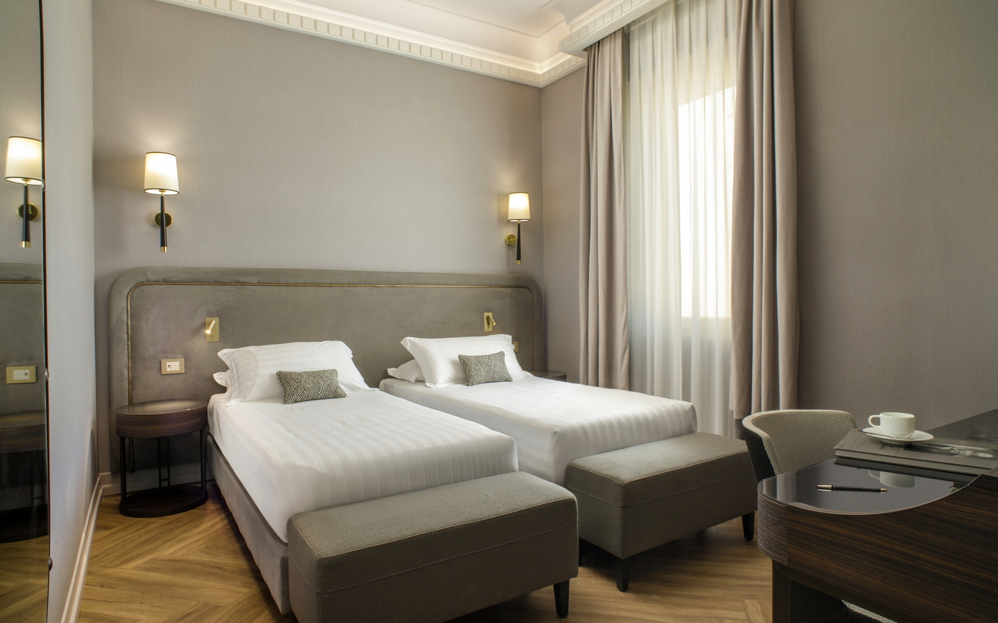 Helles Hotelzimmer mit zwei Einzelbetten, Nachttischlampen und Schreibtisch.