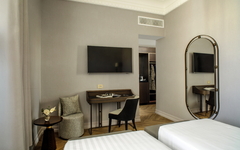 Modernes Hotelzimmer mit Doppelbett, Schreibtisch, großem Spiegel und Fernseher an der Wand.