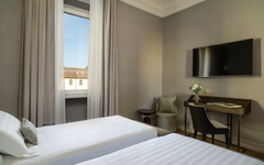Hotelzimmer mit zwei Einzelbetten, Schreibtisch, Stuhl und Flachbildfernseher an der Wand.
