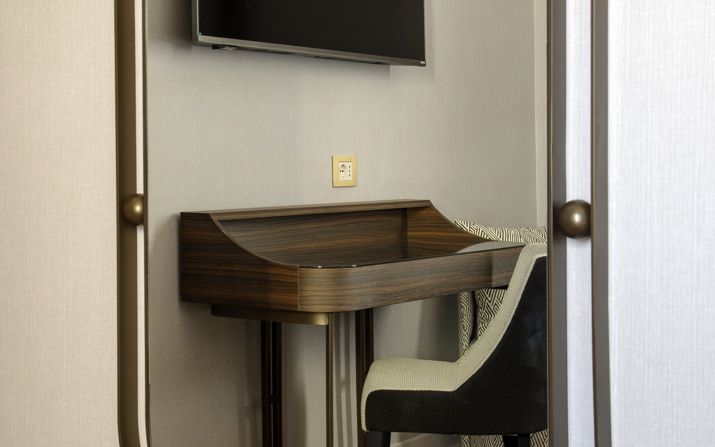 Spiegelreflexion eines Schreibtischs mit Stuhl und Fernseher an der Wand