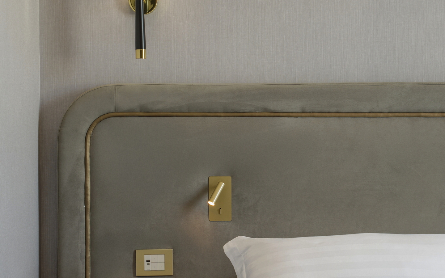 Hotelzimmer mit Bett, Kissen, Nachttisch und Wandlampe.