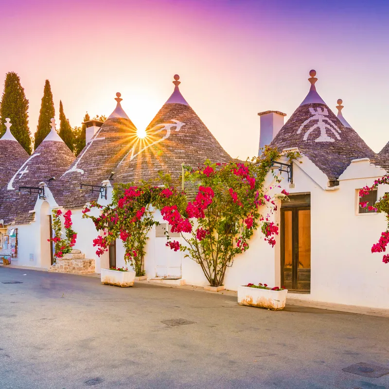Traditionelle Trulli-Häuser mit Blumen im Sonnenuntergang in Apulien, Italien.
