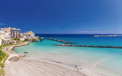 Strand von Otranto in Apulien mit blauem Meer und Gebäuden im Hintergrund.