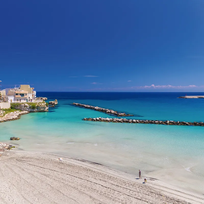 Strand von Otranto in Apulien mit blauem Meer und Gebäuden im Hintergrund.