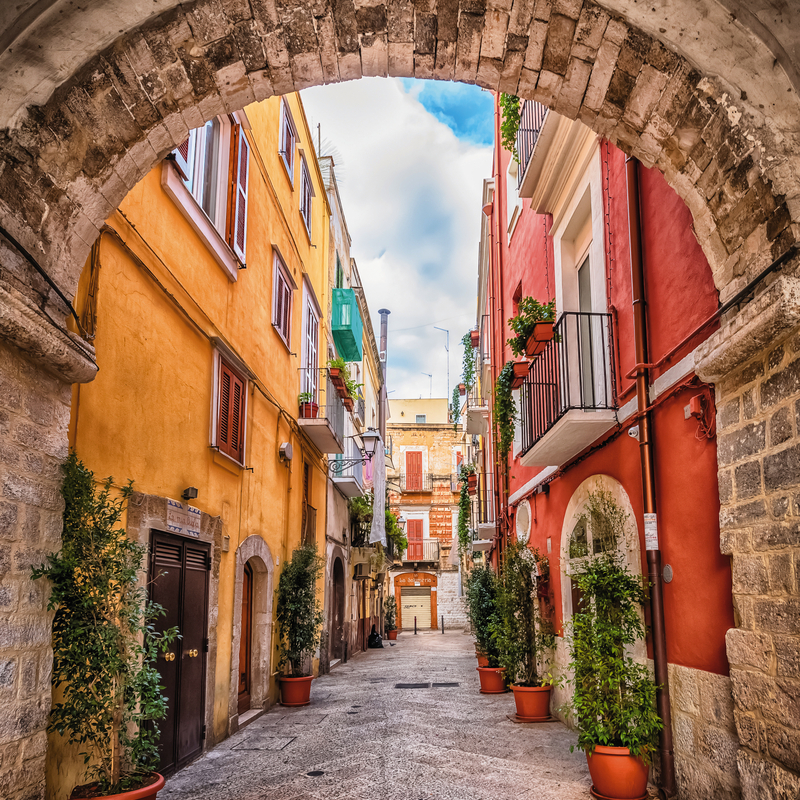 Schmale, gepflasterte Gasse mit bunten Häusern und Pflanzen in Bari, Italien.