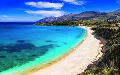 Küste mit türkisblauem Meer und sandigem Strand vor einer Bergkulisse.