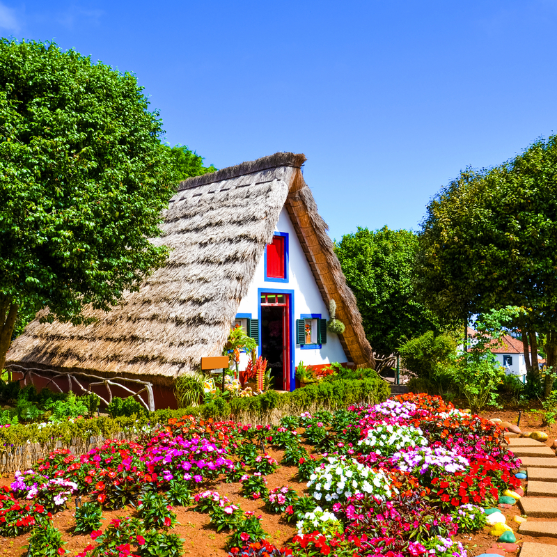 Traditionelles A-förmiges Haus mit Strohdach, umgeben von buntem Garten und Bäumen.